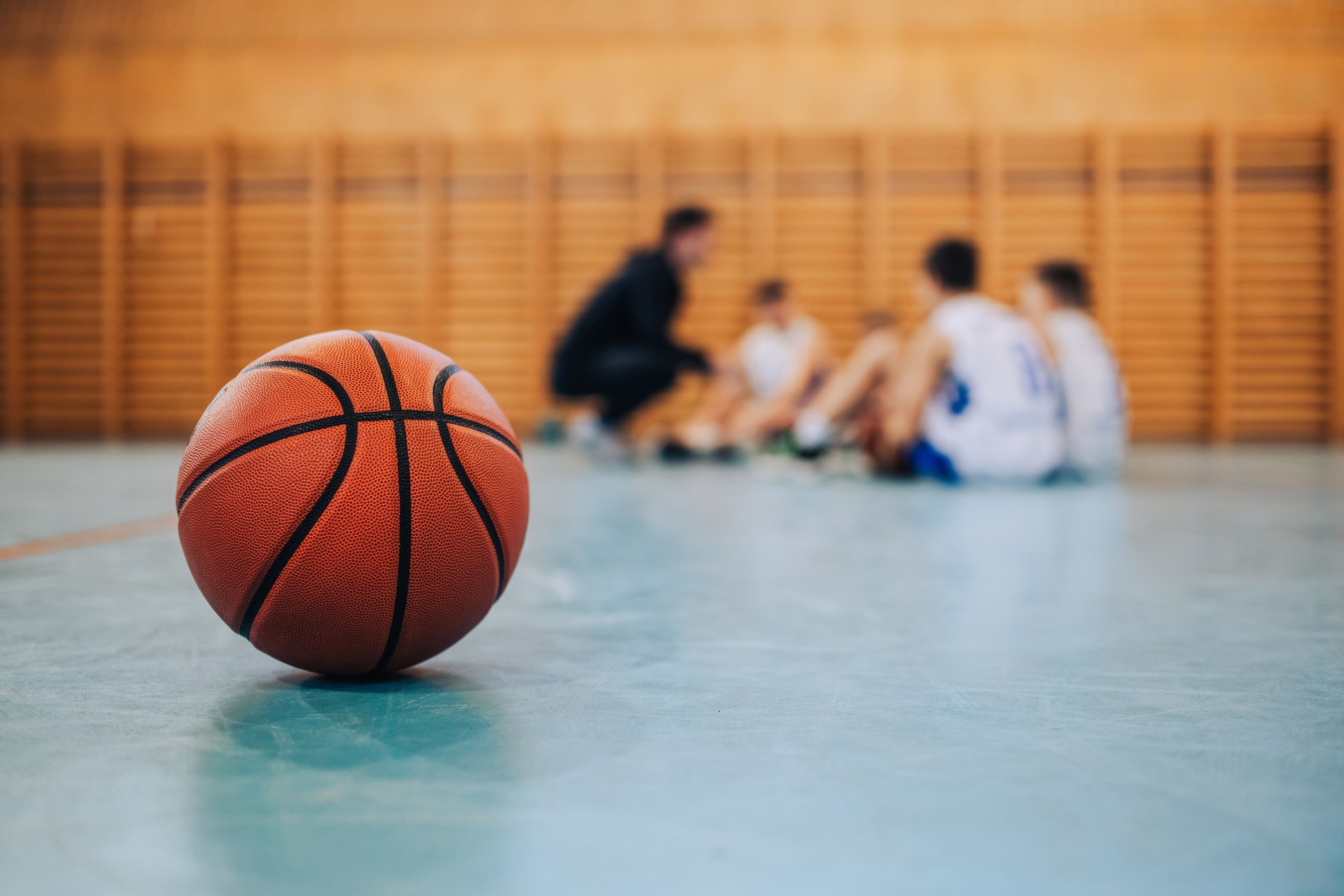 A basketball on court with junior team in blurry background.